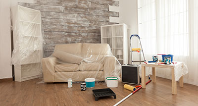 living room with a sofa covered in plastic sheets surrounded by painting supplies and furniture ready for a renovation process that can take 5 days